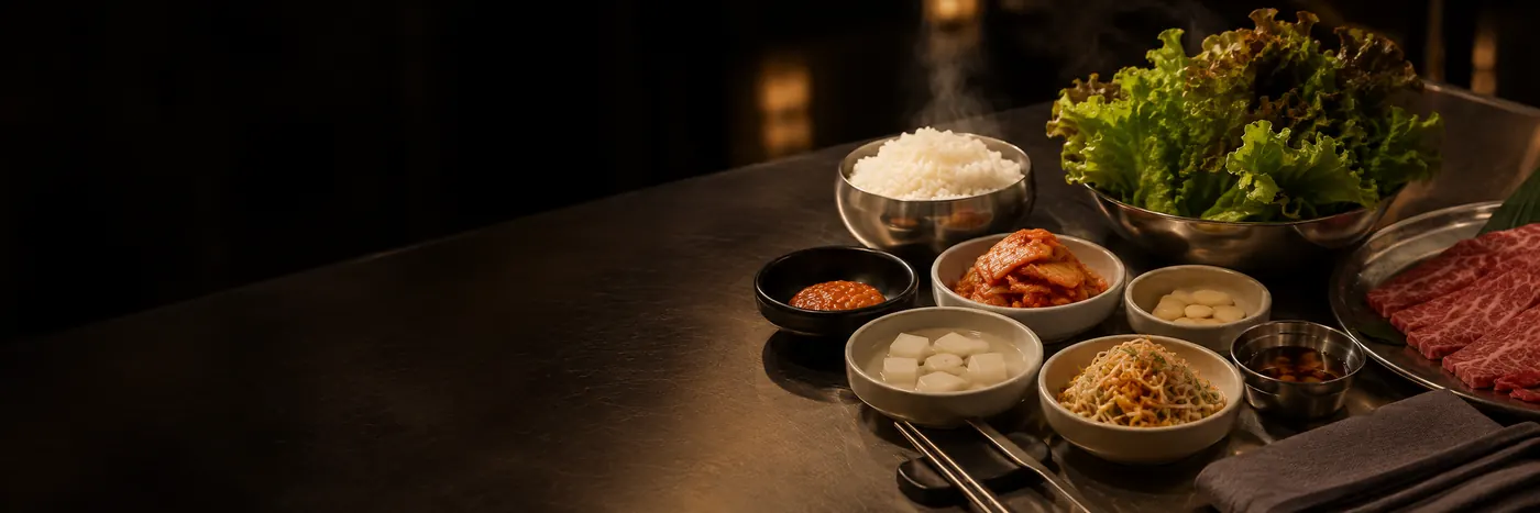 A Korean barbecue spread with steamed rice, kimchi, banchan, lettuce wraps, and marbled beef